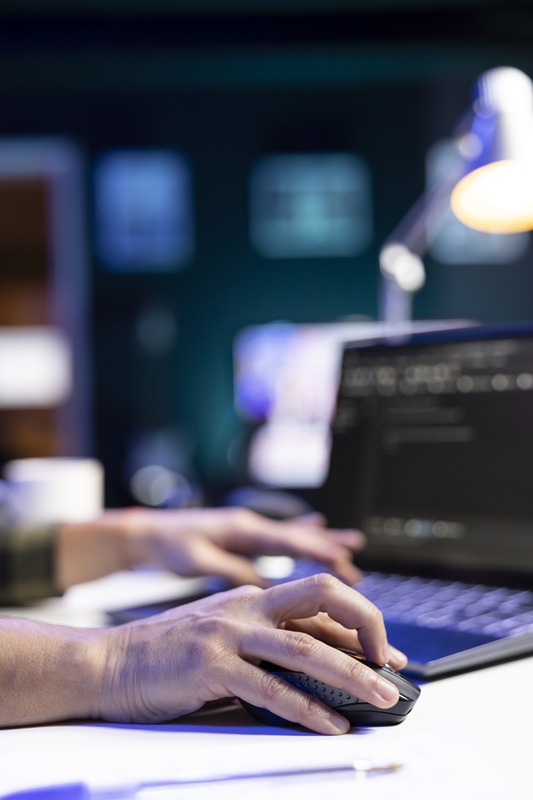 Closeup of person coding at his desk, typing on digital laptop and using a mouse, managing database systems. Working independently, an individual excels in cyber security and machine learning.